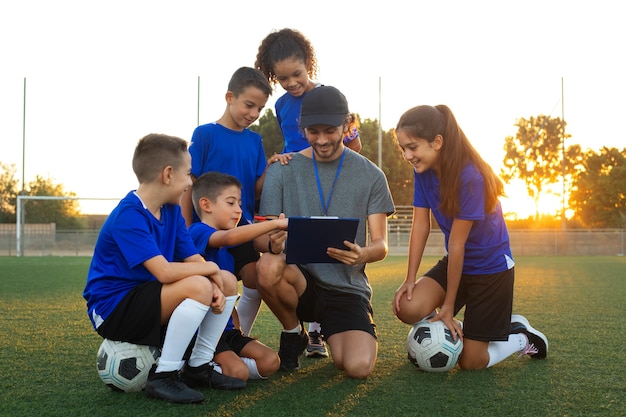 Foto gratuita entrenador de fútbol enseñando a los niños vista frontal