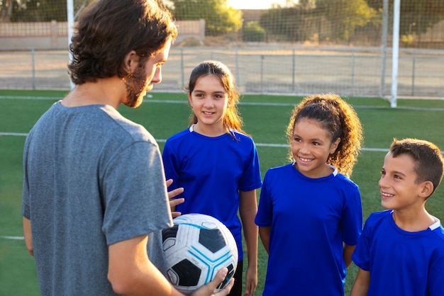 Entrenador de fútbol hablando con niños vista lateral