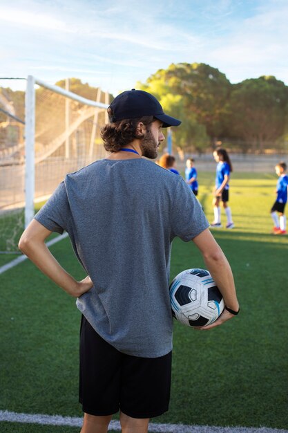 Entrenador de fútbol sosteniendo la pelota vista posterior