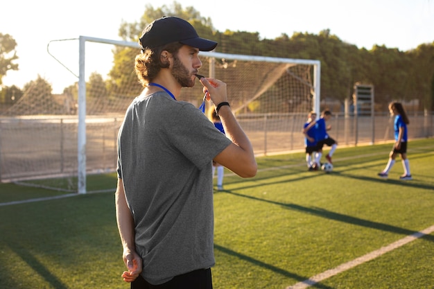 Entrenador de fútbol de tiro medio ayudando a los niños