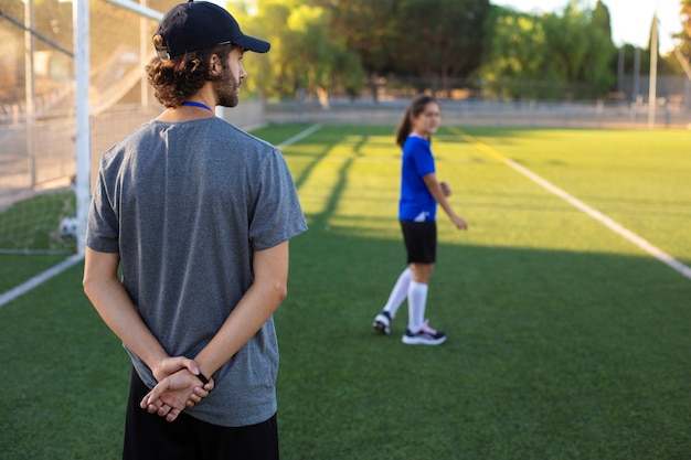 Entrenador de fútbol de vista trasera ayudando a los niños