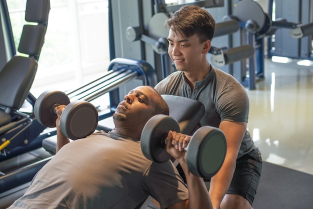 Entrenador y hombre tumbado y levantando pesas en gimnasio