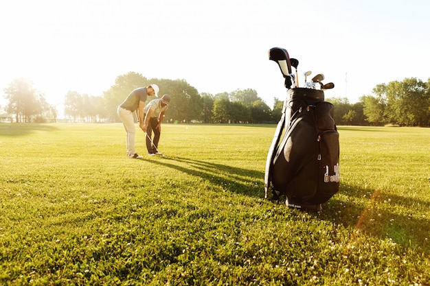 Foto gratuita entrenador masculino senior enseñando al joven deportista a jugar al golf