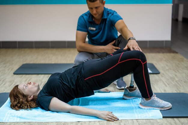 Entrenador personal que ayuda a una mujer con discapacidad en su entrenamiento. Centro de Rehabilitación Deportiva con fisioterapeutas y pacientes trabajando juntos hacia la curación.