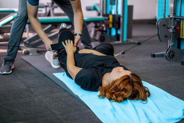 Entrenador personal que ayuda a una mujer con discapacidad en su entrenamiento. Centro de Rehabilitación Deportiva con fisioterapeutas y pacientes trabajando juntos hacia la curación.