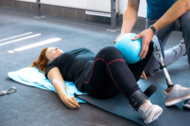 Entrenador personal que ayuda a una mujer con discapacidad en su entrenamiento. Centro de Rehabilitación Deportiva con fisioterapeutas y pacientes trabajando juntos hacia la curación.