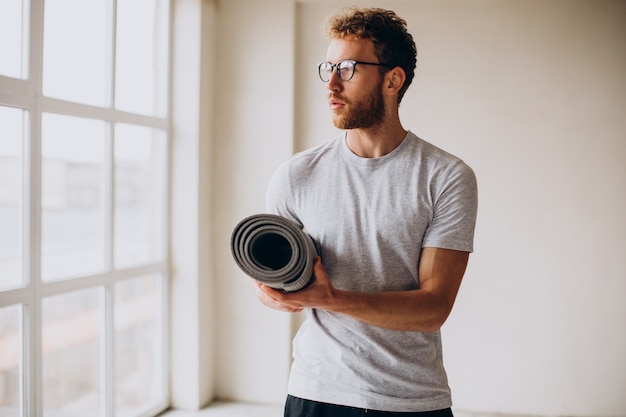 Foto gratuita entrenador de yoga de pie con estera junto a la ventana