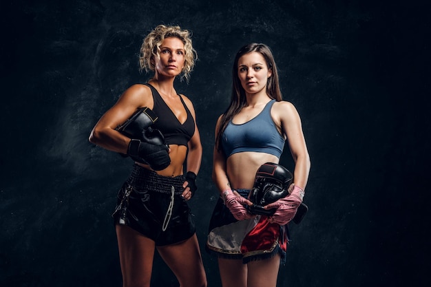 La entrenadora de boxeo experimentada y su joven estudiante posan para el fotógrafo en un estudio fotográfico oscuro.