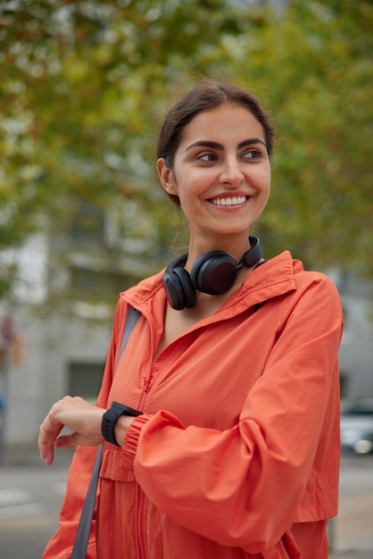 Foto gratuita la entrenadora o instructora de fitness feliz espera a que el entrenamiento comience a controlar el reloj inteligente durante las poses de entrenamiento con instalaciones deportivas, caminatas en el parque y mira hacia otro lado. concepto de ejercicio y electrónica.