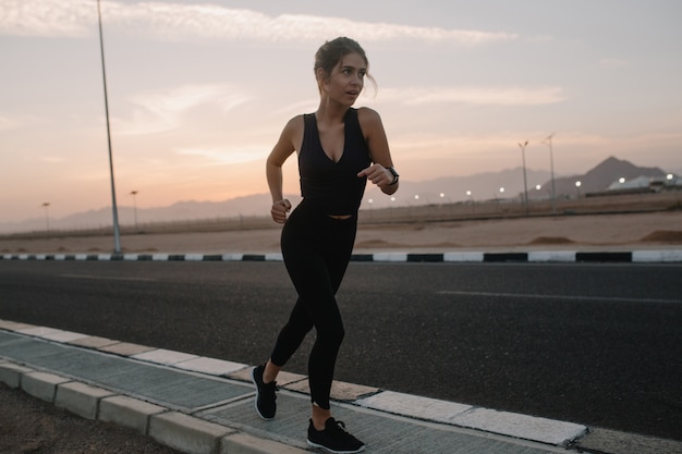 Entrenamiento, corriendo en la carretera en la soleada mañana de una mujer hermosa. Verano, deportista fuerte, energía, motivación, estilo de vida saludable, entrenamiento, felicidad, disfrutar del deporte