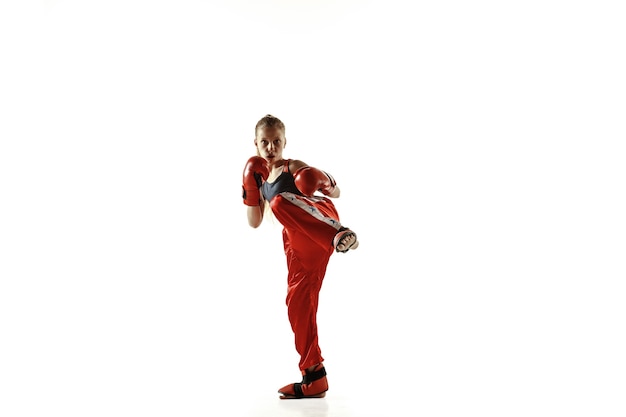 Entrenamiento de luchador de kickboxing femenino joven aislado en la pared blanca. Chica rubia caucásica en ropa deportiva roja practicando artes marciales. Concepto de deporte, estilo de vida saludable, movimiento, acción, juventud.