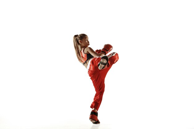Entrenamiento de luchador de kickboxing femenino joven aislado en la pared blanca. Chica rubia caucásica en ropa deportiva roja practicando artes marciales. Concepto de deporte, estilo de vida saludable, movimiento, acción, juventud.