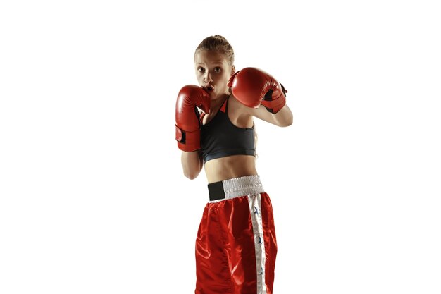 Entrenamiento de luchador de kickboxing femenino joven aislado en la pared blanca. Chica rubia caucásica en ropa deportiva roja practicando artes marciales. Concepto de deporte, estilo de vida saludable, movimiento, acción, juventud.