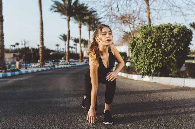 Entrenamiento en mañana soleada de hermosa mujer joven en la calle con palmeras. Ciudad tropical, resort, estado de ánimo alegre, estilo de vida saludable, estiramiento, ejercicio, figura atractiva