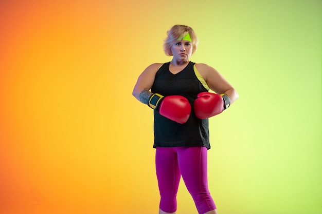 Entrenamiento del modelo femenino caucásico joven del tamaño extra grande en fondo anaranjado degradado en luz de neón.