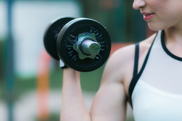 Entrenamiento de mujer con mancuerna al aire libre, bíceps ejercicio primer plano