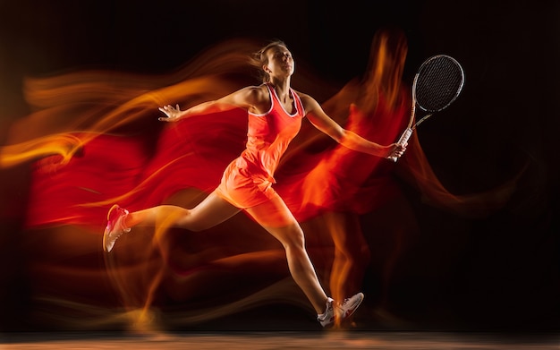 Entrenamiento de tenista profesional aislado sobre fondo negro de estudio en luz mixta. Mujer en traje deportivo practicando.