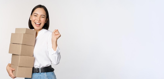 Entusiasta chica coreana compradora sosteniendo cajas de entrega y sonriendo feliz de pie sobre backgr blanco