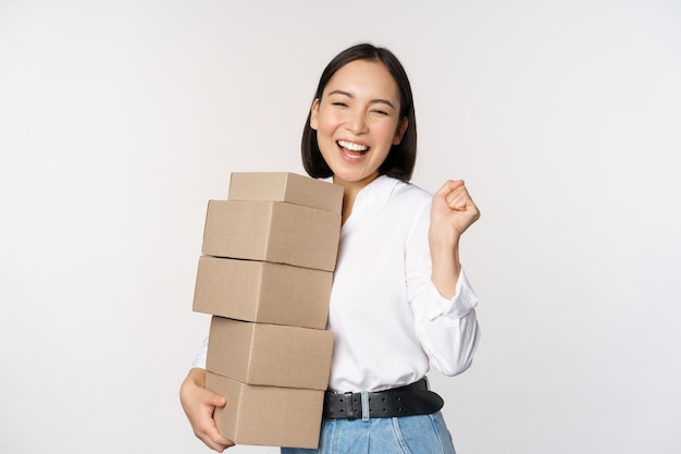 Entusiasta compradora coreana sosteniendo cajas de entrega y sonriendo feliz de pie sobre fondo blanco.