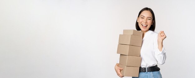 Entusiasta compradora coreana sosteniendo cajas de entrega y sonriendo feliz de pie sobre fondo blanco.