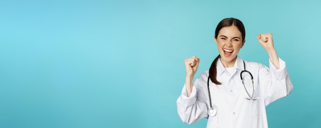 Foto gratuita entusiasta doctora mujer regocijándose de ganar y celebrando lograr el objetivo de pie en bata blanca agai