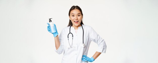 Entusiasta doctora en uniforme que muestra jabón de manos desinfectante covid19 prevención de pie sobre fondo blanco