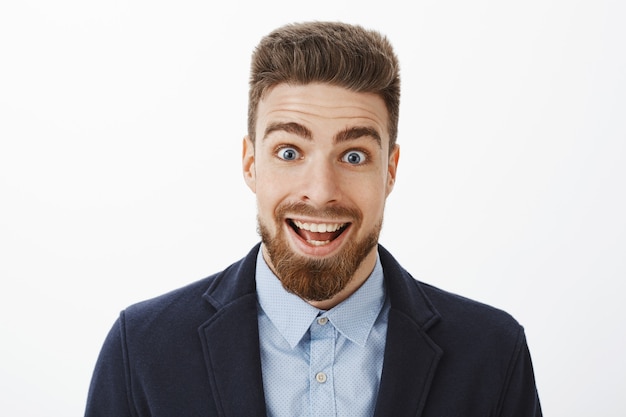 Entusiasta emocionado y sorprendido feliz apuesto hombre con barba y profundos ojos azules, sonriendo ampliamente por el asombro, ojos que brotan, deleitado sintiéndose impresionado y asombrado con buenas noticias.