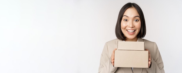 Entusiasta empresaria asiática dando cajas de pedidos de clientes de pie contra el fondo blanco.