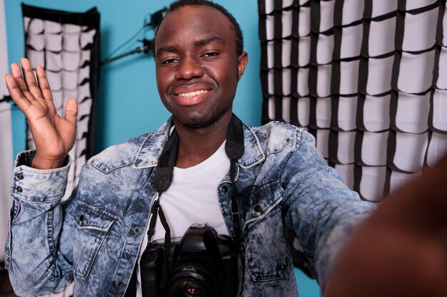 Entusiasta de la fotografía haciéndose una foto junto a softboxes y focos. Director de estudio de producción confiado tomando una foto selfie mientras está de pie junto a un equipo de filmación profesional.