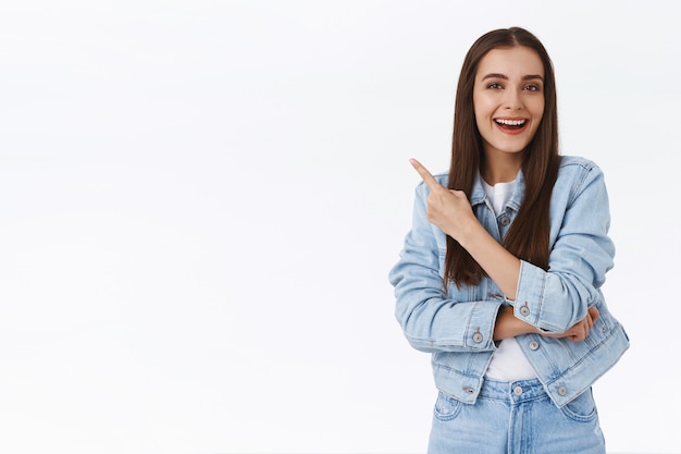 Foto gratuita entusiasta joven atractiva mujer caucásica riendo sobre un anuncio impresionante, apuntando hacia la esquina superior izquierda, mira impresionado y complacido, sonriendo a la cámara mientras discuten una promoción genial, fondo blanco.