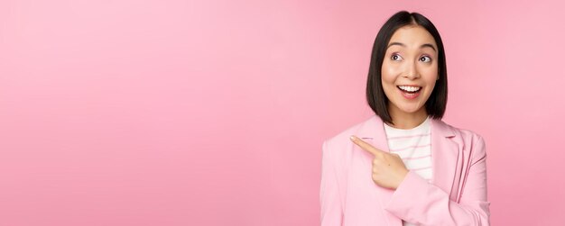 Entusiasta joven empresaria asiática empleada de oficina señalando con el dedo a la izquierda mirando el anuncio publicitario