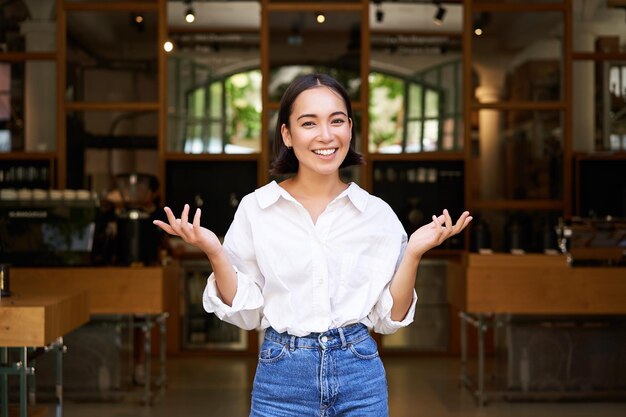 Entusiasta joven empresaria chica asiática mostrando su negocio levantando las manos y sonriendo standi