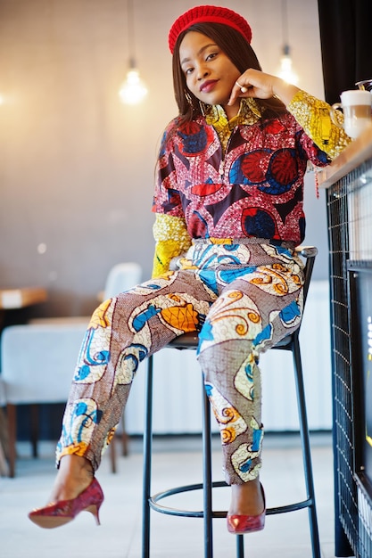 Entusiasta mujer afroamericana vestida de moda con boina roja relajándose en un acogedor café sentado en el mostrador del bar