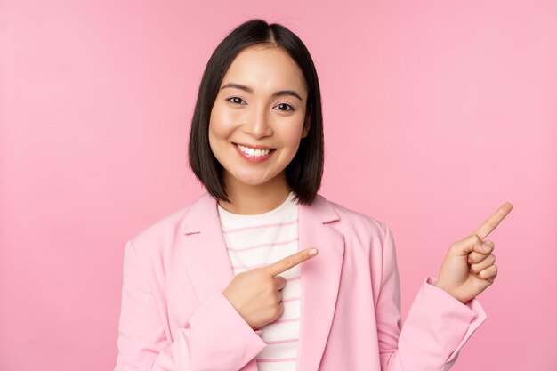 Entusiasta mujer de negocios profesional vendedora señalando con el dedo a la derecha mostrando publicidad o el logotipo de la empresa a un lado posando sobre fondo rosa