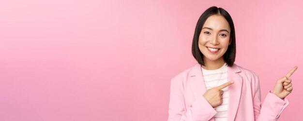 Entusiasta mujer de negocios profesional vendedora señalando con el dedo a la derecha mostrando publicidad o el logotipo de la empresa a un lado posando sobre fondo rosa