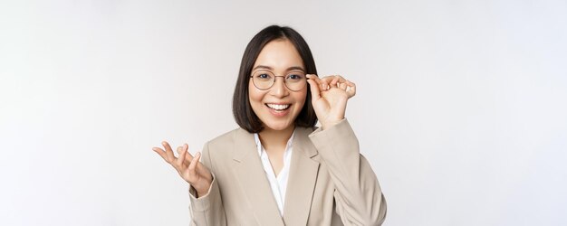 Entusiasta vendedora asiática con gafas sonriendo y riendo mirando asombrada a la cámara de pie en b