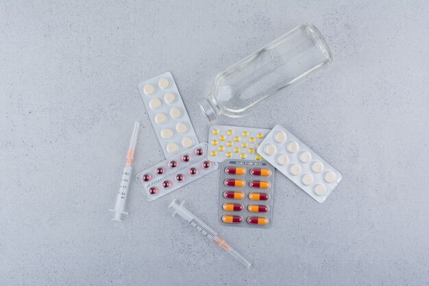 Envases de medicamentos, ampollas y jeringas sobre superficie de mármol.