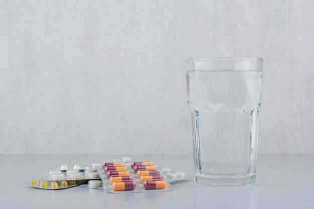 Envases surtidos de cápsulas y pastillas con vaso de agua.