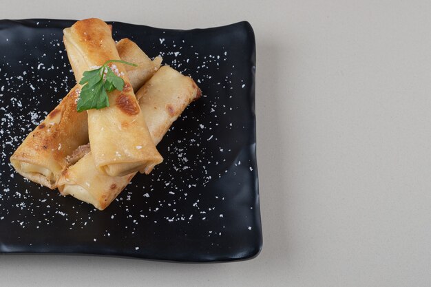 Envoltorios de panqueques rellenos en un plato negro sobre fondo de mármol.