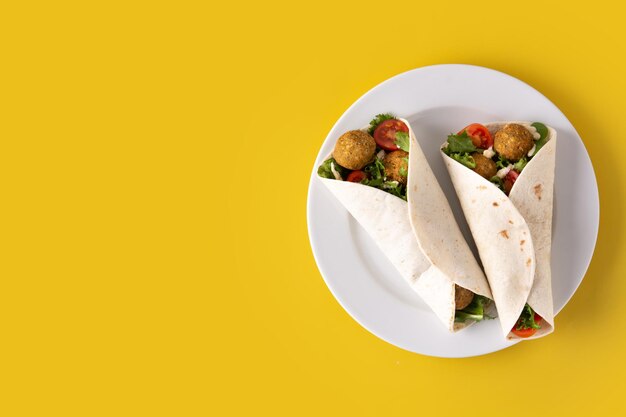 Envoltura de tortilla con falafel y verduras sobre fondo amarillo