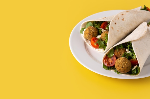 Foto gratuita envoltura de tortilla con falafel y verduras sobre fondo amarillo