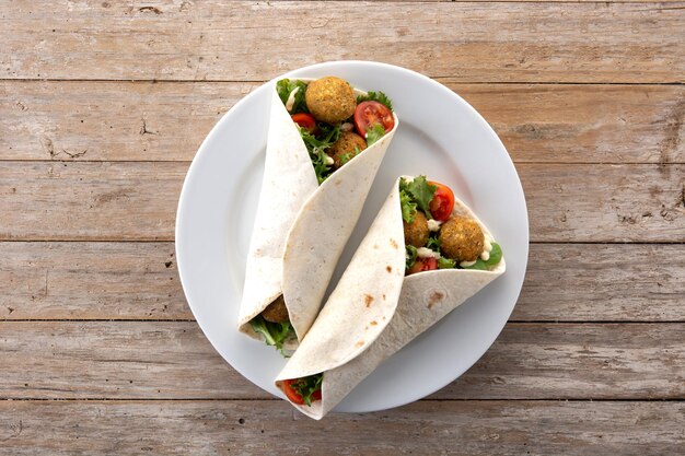 Envoltura de tortilla con falafel y verduras sobre mesa de madera