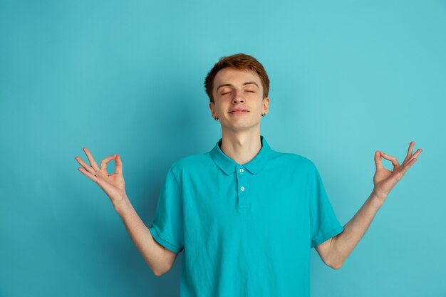 Equilibrado, tranquilo. Retrato moderno del hombre joven caucásico aislado en la pared azul, monocromo. Hermoso modelo masculino. Concepto de emociones humanas, expresión facial, ventas, publicidad, moda.