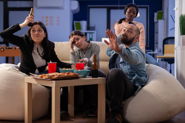 Equipo de amigos multiétnicos que pierden el juego de televisión en la consola después del trabajo en la oficina