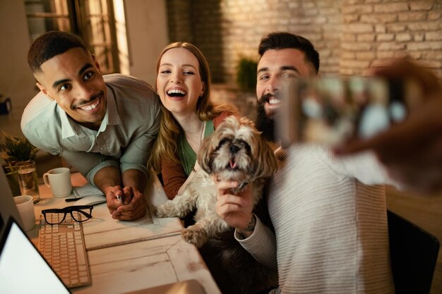 Equipo de colegas de negocios felices usando teléfonos inteligentes y tomando selfie con un perro