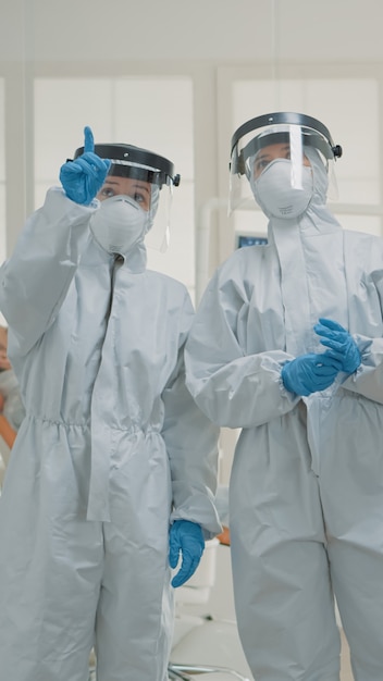 Equipo de dentistas caucásicos con trajes de materiales peligrosos discutiendo la prevención