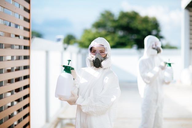 Equipo de especialistas en desinfección en equipo de protección personal (EPI) traje, guantes, mascarilla y protector facial, limpieza del área de cuarentena con una botella de spray desinfectante presurizado para eliminar el covid-19