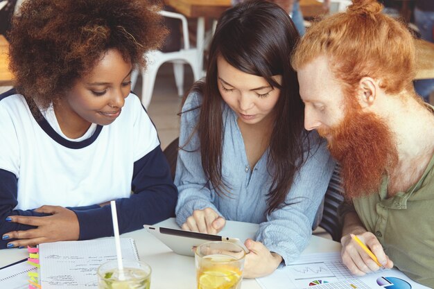 Equipo de jóvenes de diversas etnias haciendo una lluvia de ideas, discutiendo planes de negocios e ideas de su proyecto común, luciendo entusiastas.