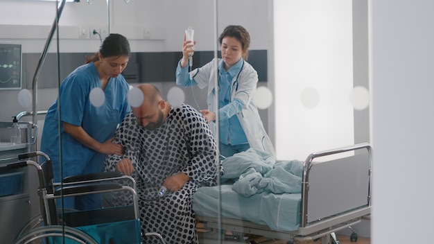 Equipo médico ayudando a paciente enfermo con fractura de lesión en la pierna poniendo en silla de ruedas