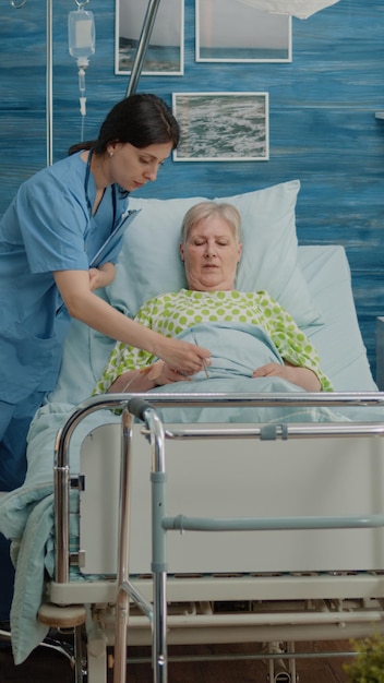 Equipo médico que examina a un paciente enfermo en una cama de hospital en un hogar de ancianos. Médico que usa una tableta digital mientras la enfermera pone el oxímetro en la mano de una mujer jubilada para un chequeo.